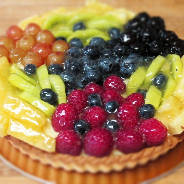 Close-up of a vibrant fruit tart from L.A. Bakery, topped with blueberries, raspberries, kiwi, and grapes.