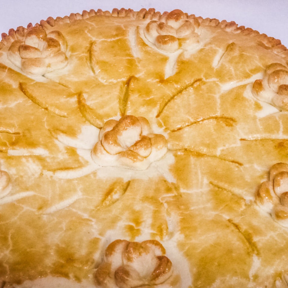 Close-up of a golden baked pastry decorated with braided edges, floral dough motifs, and scored patterns.