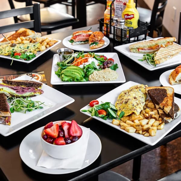 A table laden with various L.A. Bakery cafe dishes, including sandwiches, omelets, salads, and fruit.