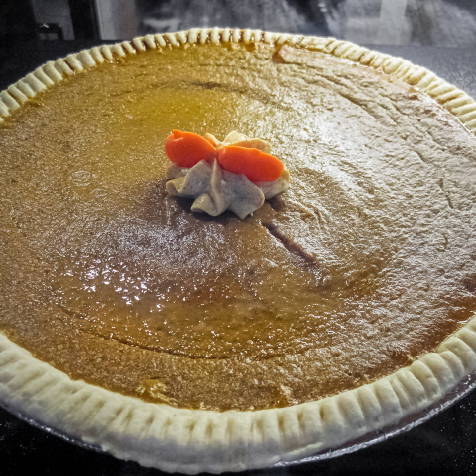 Golden custard pie with a crimped crust, topped with whipped cream and orange fruit slices.