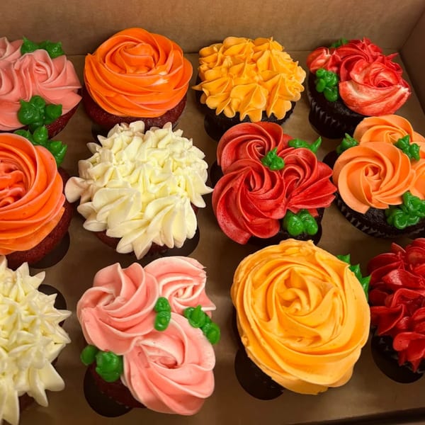 A dozen L.A. Bakery cupcakes with vibrant red, orange, pink, yellow, and white floral frosting designs.
