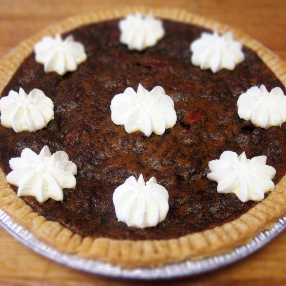 Chocolate pie with a golden crust, topped with eight white whipped cream rosettes, displayed on a foil pie plate.